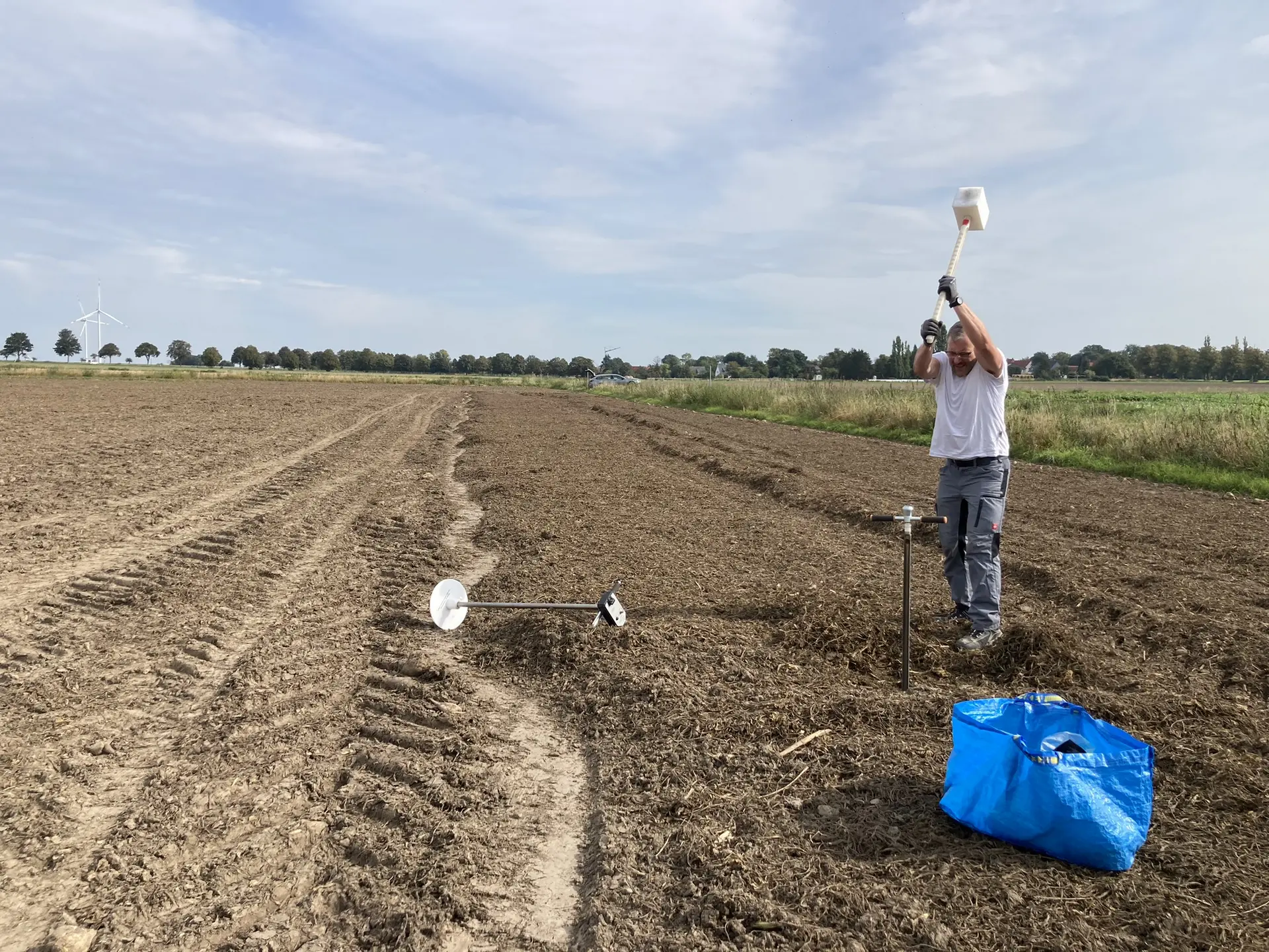 Ein Mann schlägt auf einem Feld ein Bohstock mit einem großen Hammer mit Gummispitze ein.